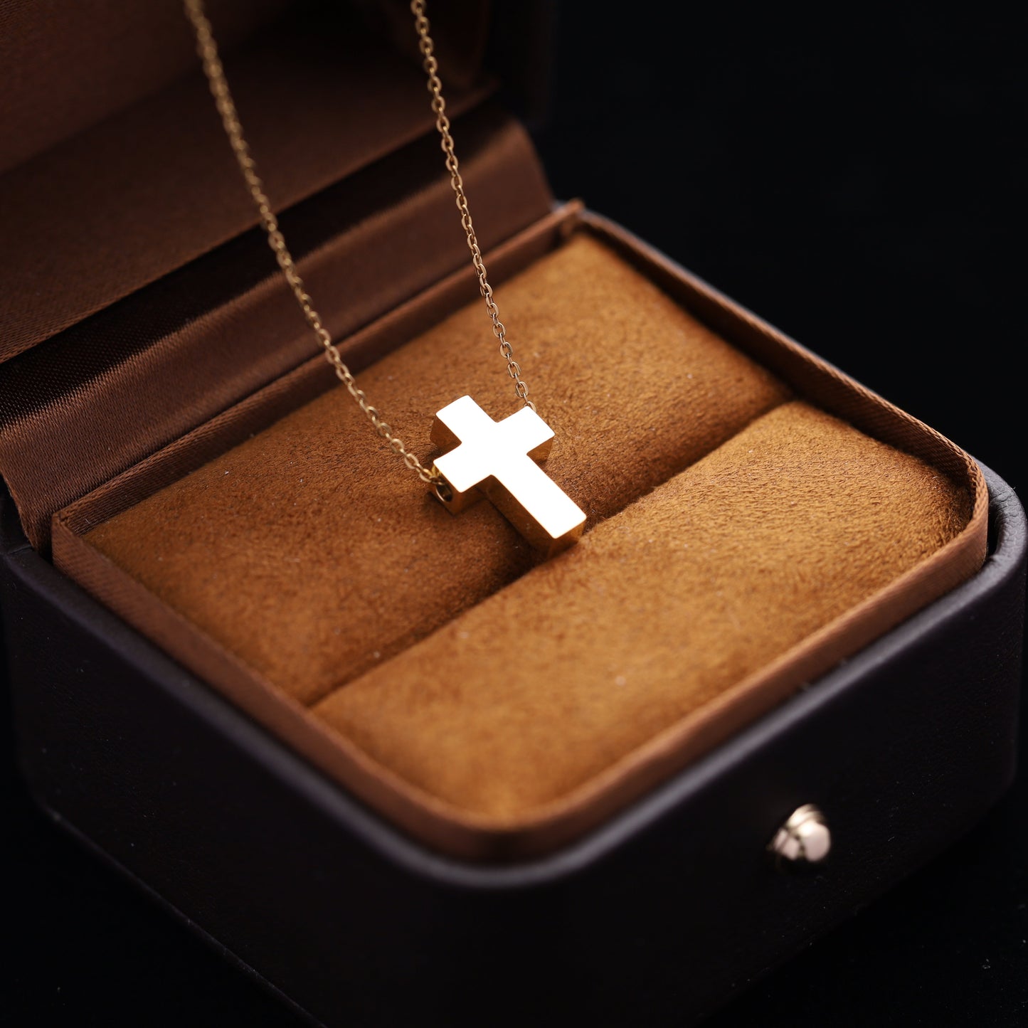 Gold stainless steel cross necklace displayed on an open palm, with a jewelry box in the background.
