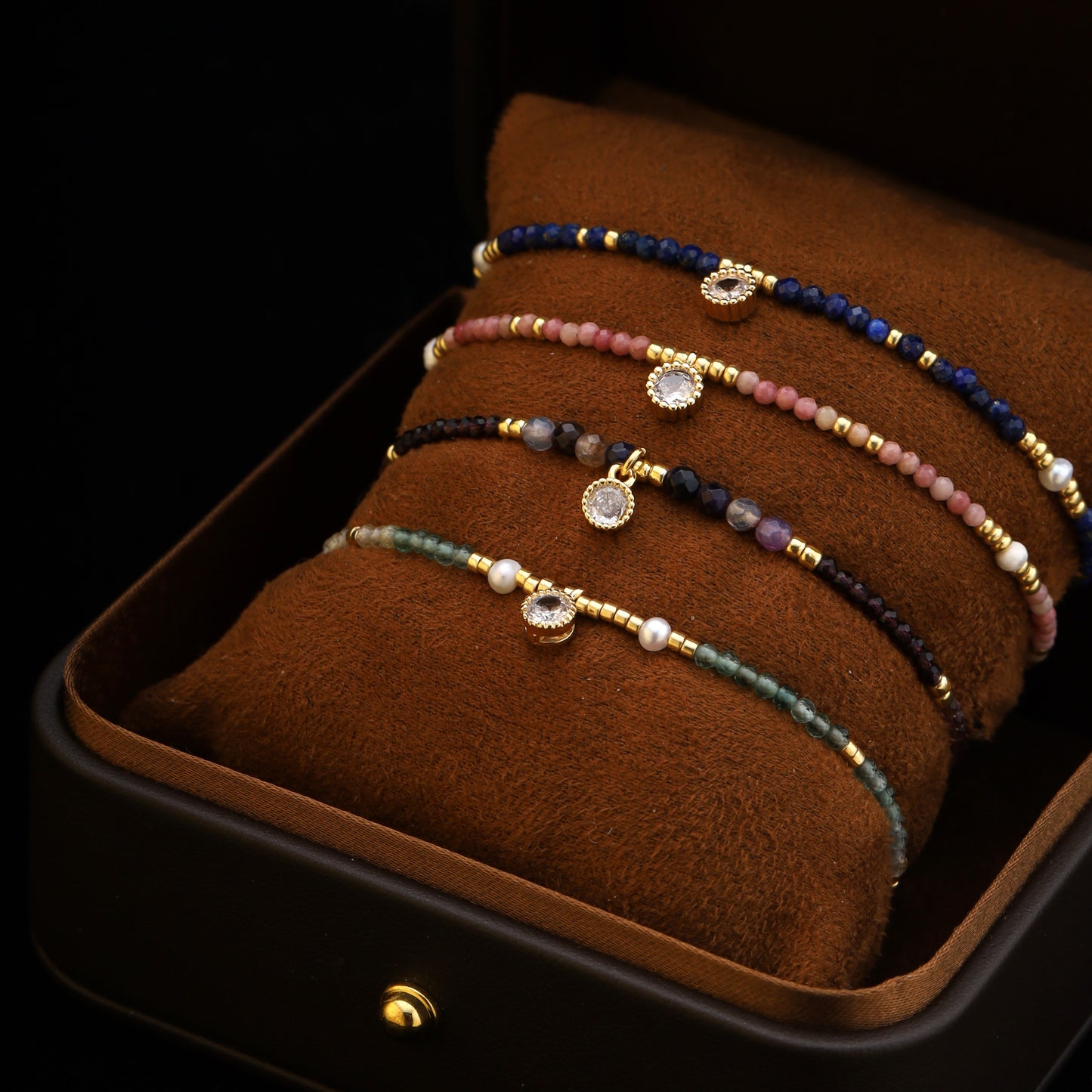 Close-up of a blue gemstone beaded bracelet with gold accents and zirconia charm, displayed in a brown velvet box.