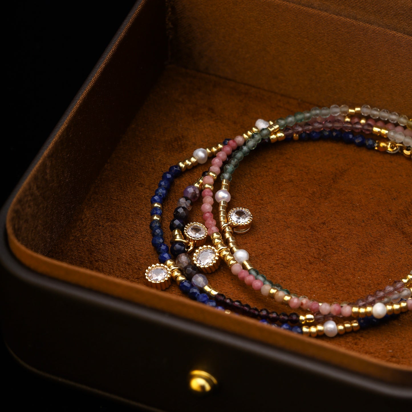Assorted gemstone bracelets laid out in a brown box showing full design and charm placement.