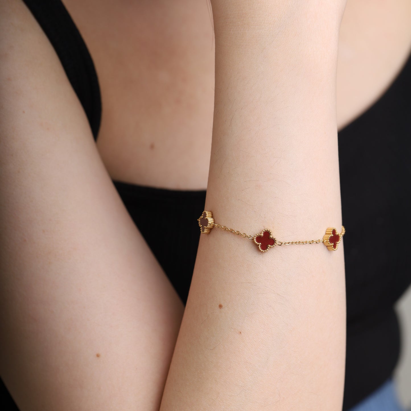 Gold-tone bracelet with red clover charms worn on wrist
