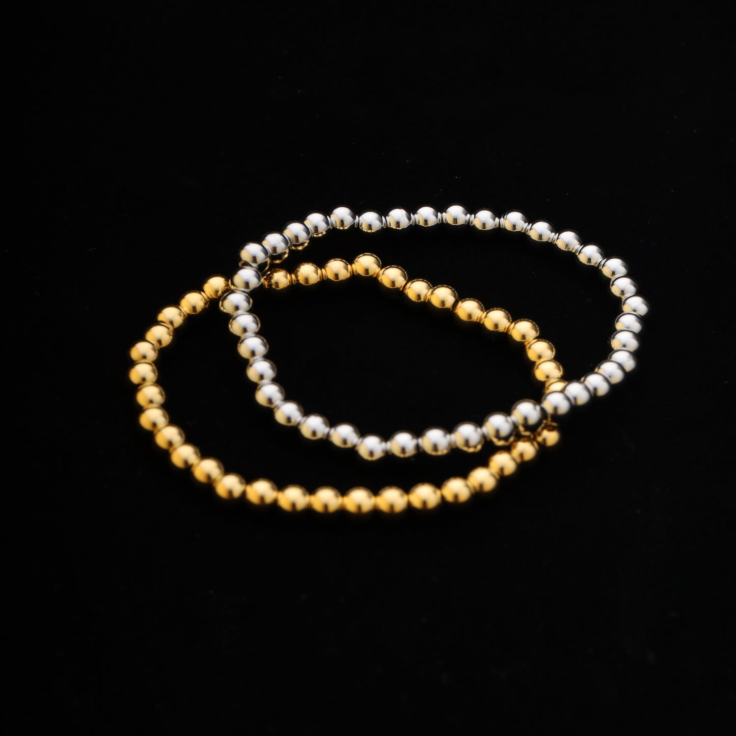 Gold and silver stainless steel beaded bracelets styled on black background