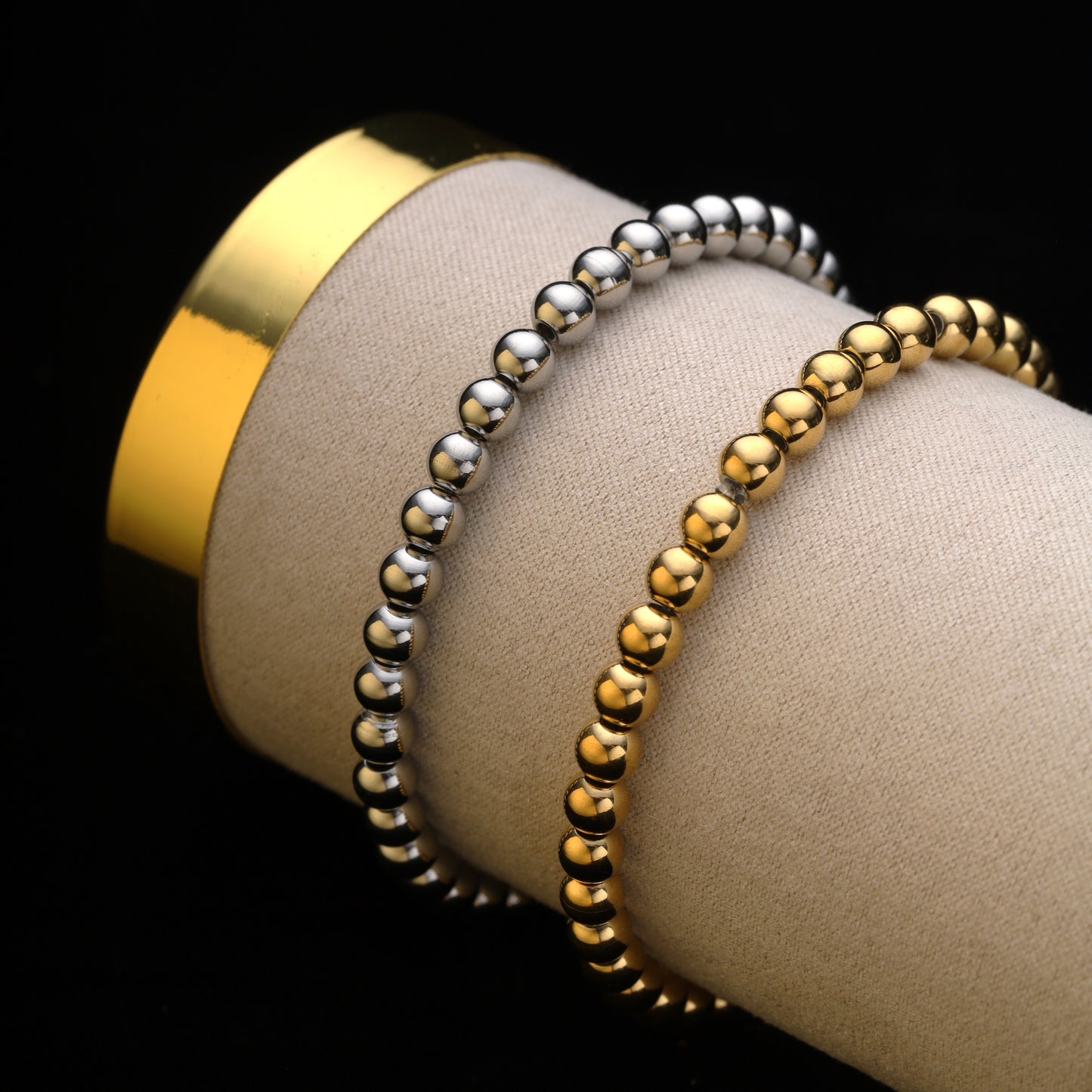 Gold and silver beaded bracelets stacked on a beige display tube