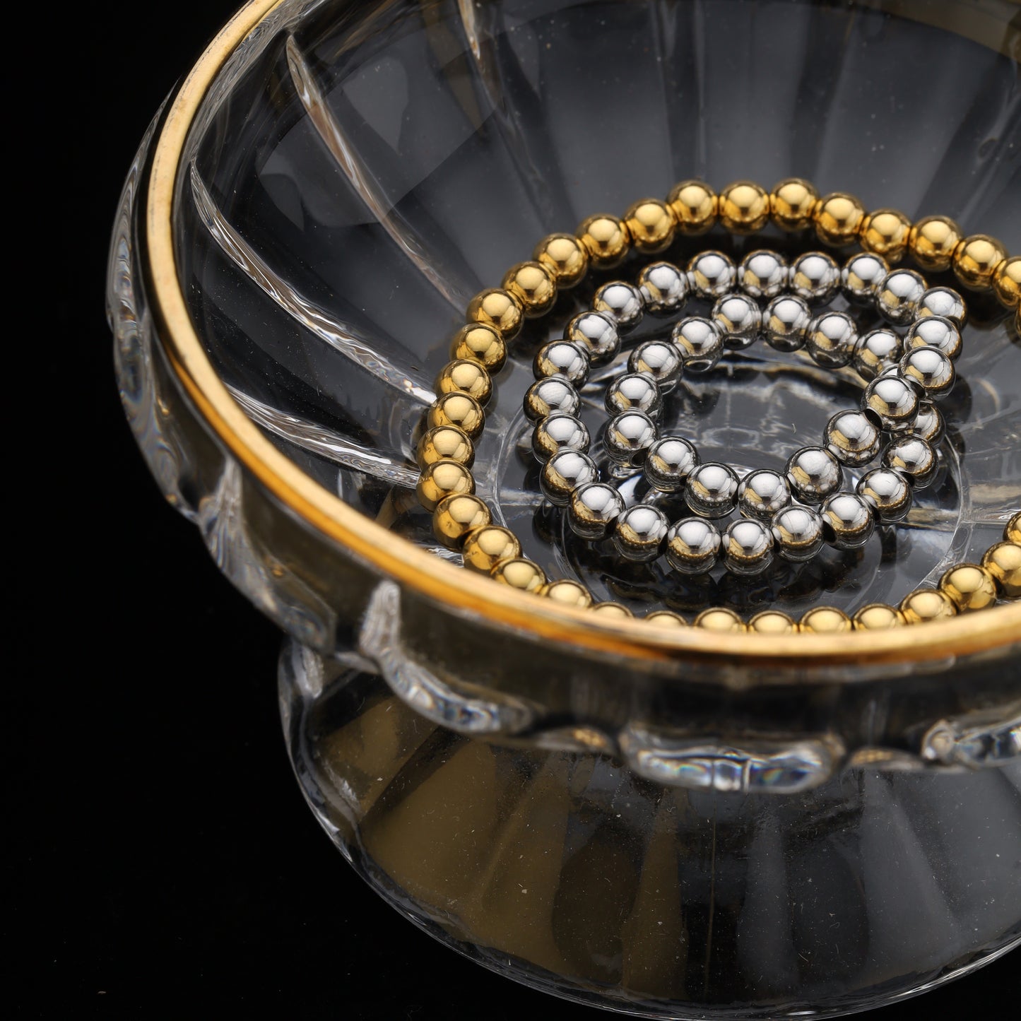 Bracelets coiled in a clear glass bowl, top view