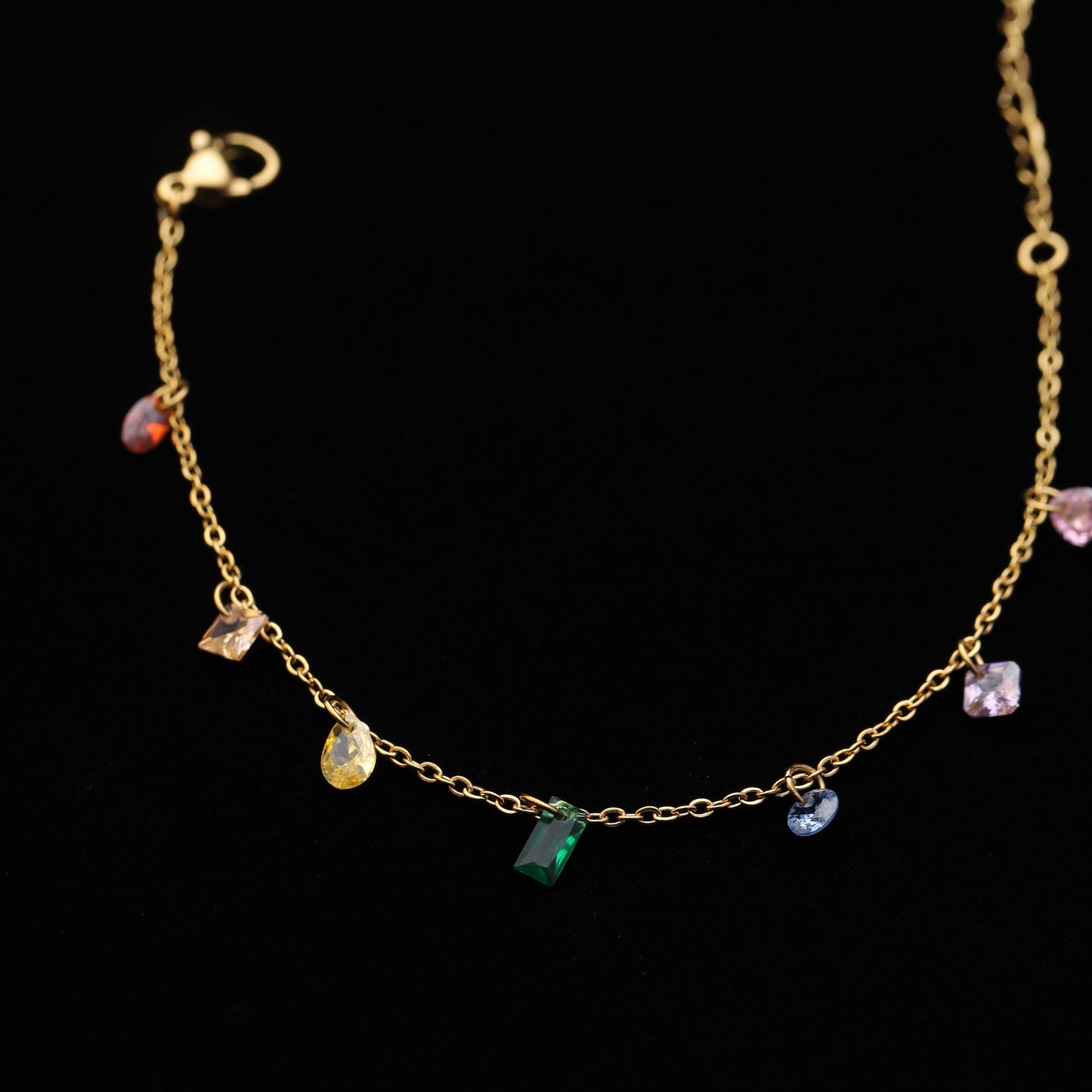Stainless steel bracelet with dangling rainbow crystals on black background