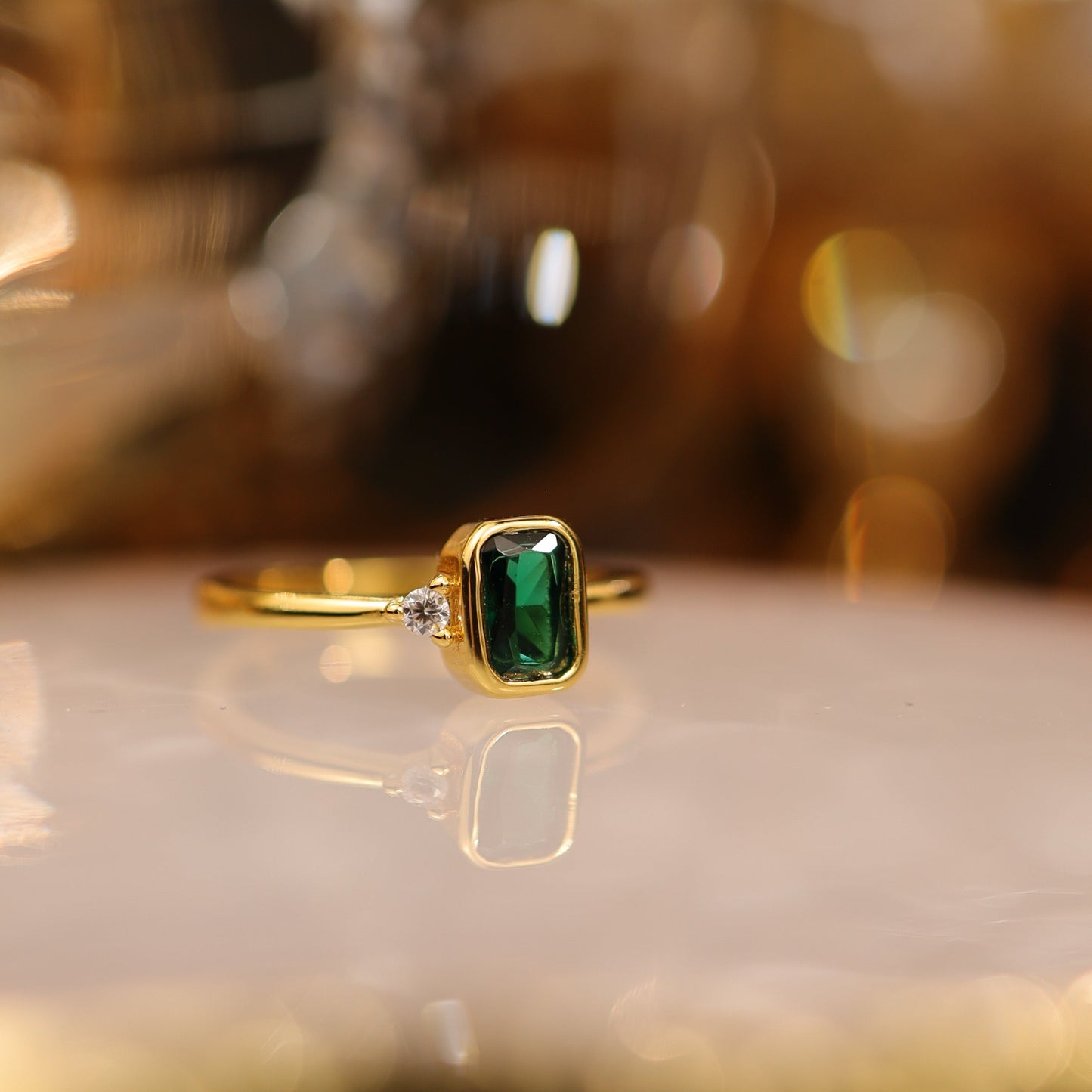 Side view of emerald green gemstone ring in gold bezel with crystal accent
