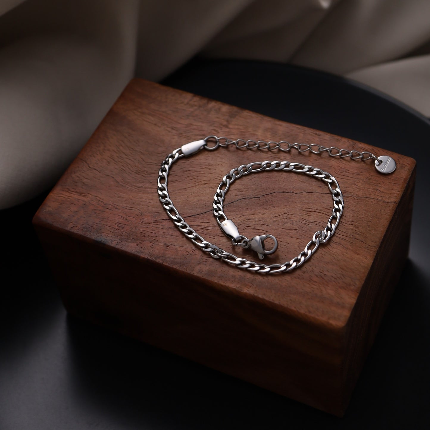 Stainless steel Figaro chain bracelet displayed on a wooden box.