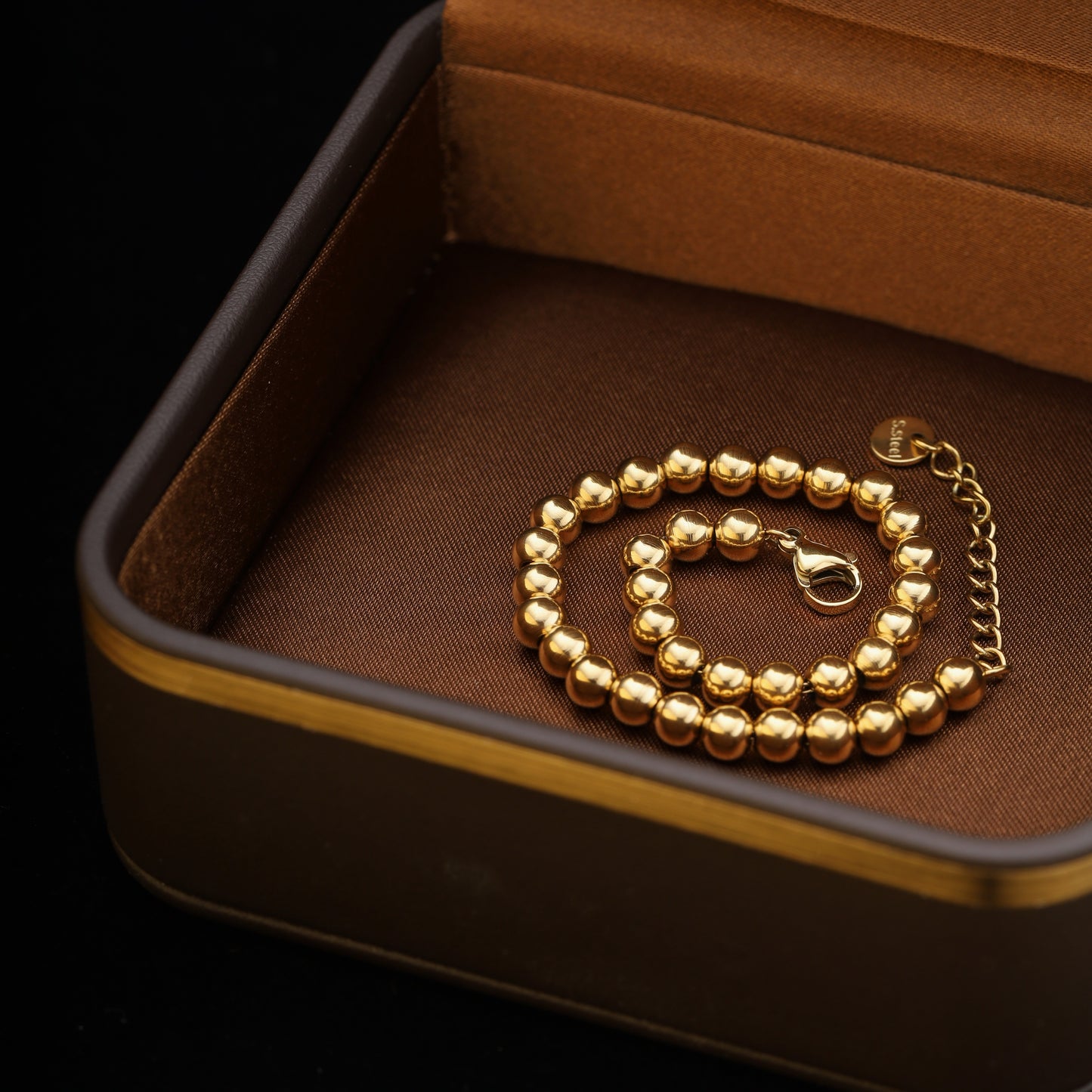 Bracelet coiled in a brown velvet jewelry box, showcasing stainless steel beads and clasp