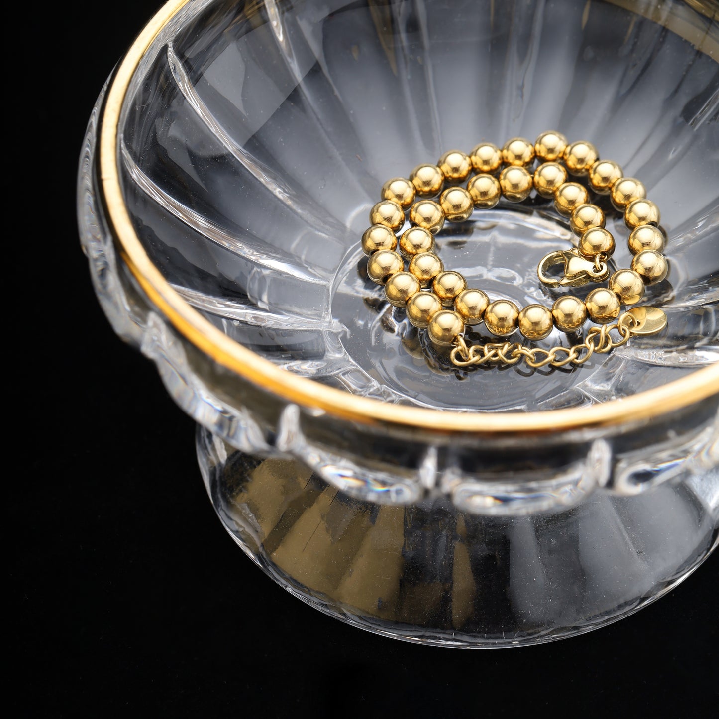 Close-up of 4mm gold beaded bracelet coiled in a glass jewelry bowl