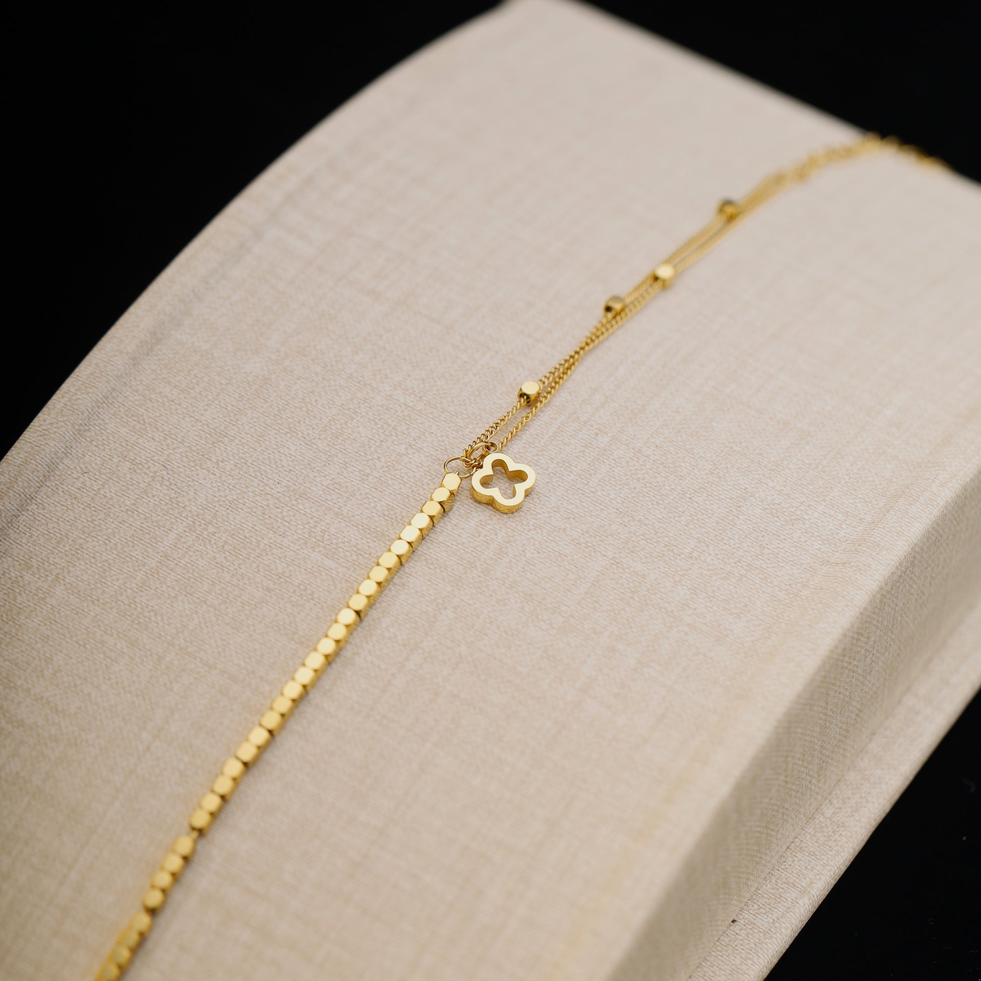 Close-up of clover charm bracelet resting on a beige jewelry display.