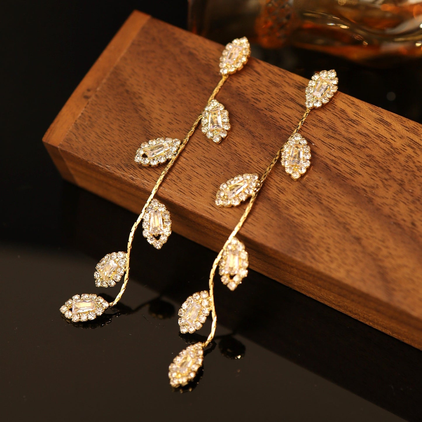 A pair of sterling silver and gold-plated leaf dangle earrings beautifully placed on a wooden display.