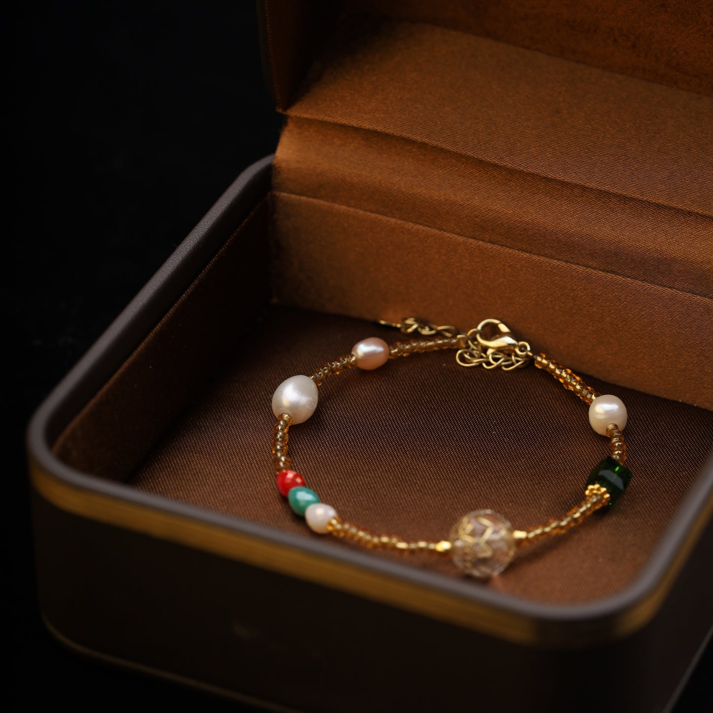 Close-up of a beaded bracelet with pearls and colorful beads inside a brown jewelry box.