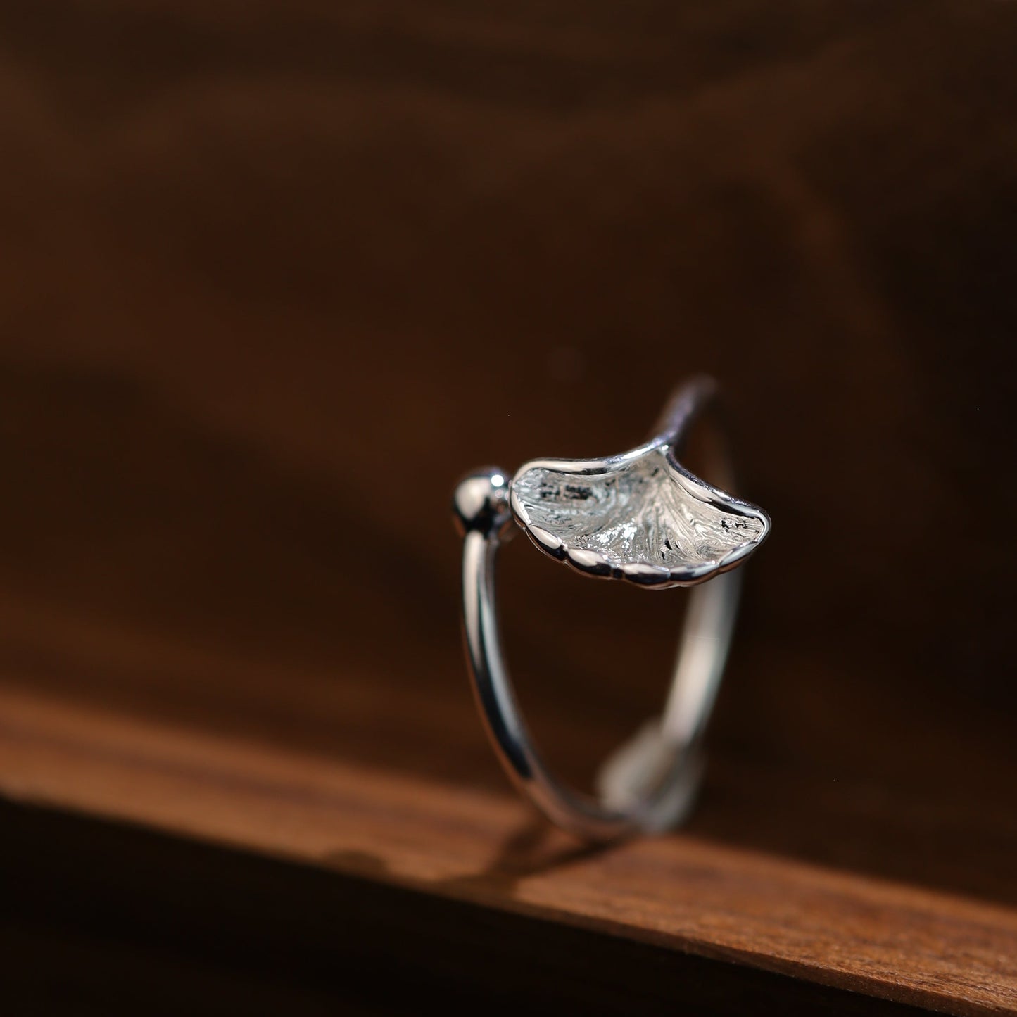 Close-up of a sterling silver ginkgo leaf ring on a wood display.