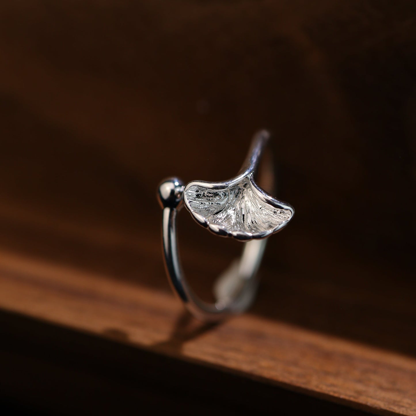 Front view of the sterling silver ginkgo leaf ring on a wood background.