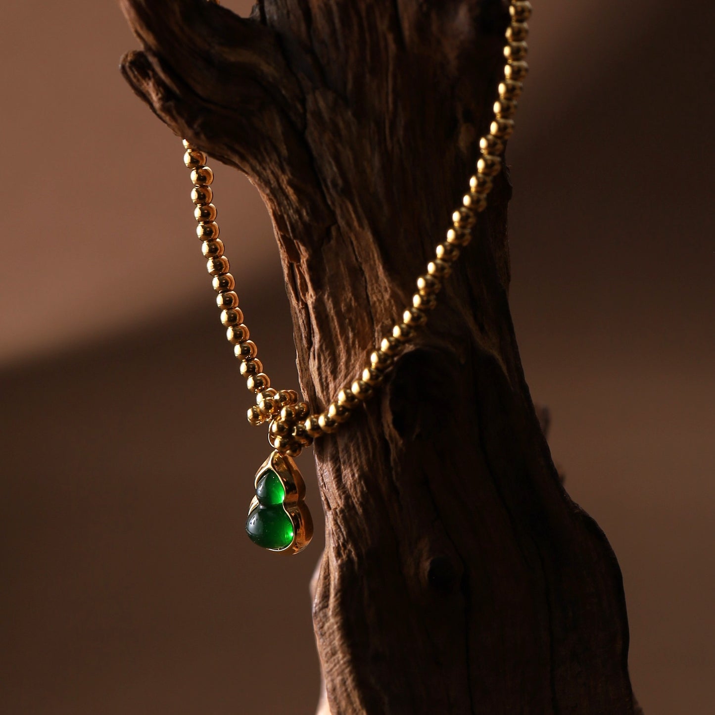 Gold beaded stretchy hulu bracelet with green charm laid flat